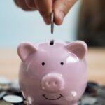1_Person-Putting-Coin-In-Piggy-Bank-At-Table.jpg