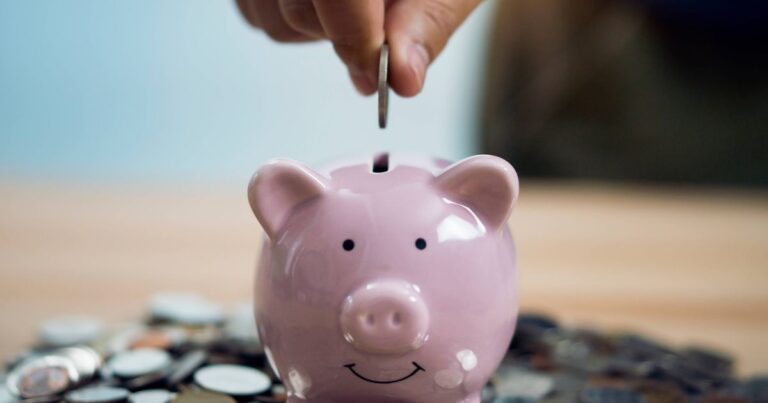 1_Person-Putting-Coin-In-Piggy-Bank-At-Table.jpg