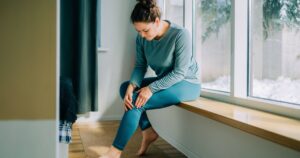 1_Woman-suffering-from-knee-pain-while-sitting-on-windowsill-at-home.jpg