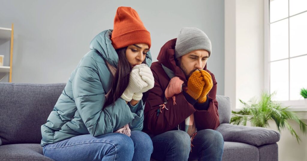 1_Young-attractive-couple-are-sitting-on-the-sofa-at-home-in-warm-clothes-and-warming-their-hands-wi.jpeg
