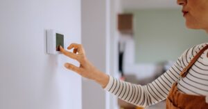 0_Casually-clothed-woman-setting-up-temperature-on-smart-thermostat-at-home.jpg