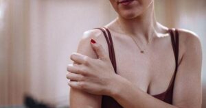 0_Close-Up-Of-Woman-Touching-Shoulder-In-A-Red-Top-Reflecting-Self-Care-And-Wellness-Moment.jpg