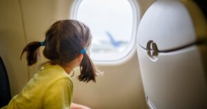 0_Little-girl-with-pigtails-sits-on-plane-staring-out-window-on-tarmac.jpg