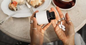 0_Hands-Holding-Pill-Bottle-Over-Table-With-Coffee-Cake-Slice-And-Casual-Morning-Scene.jpg