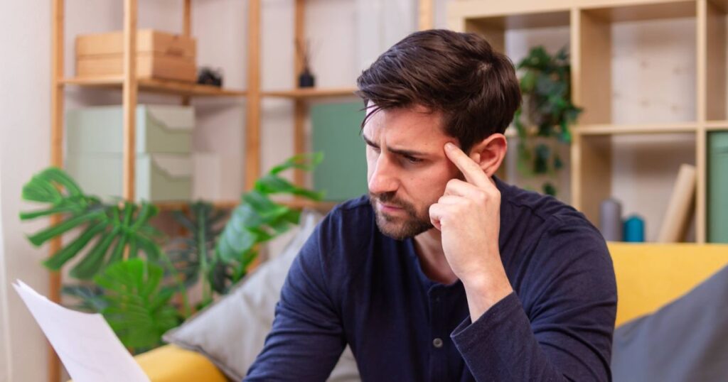 0_Young-man-sitting-on-a-sofa-reading-a-letter-having-a-headache.jpg