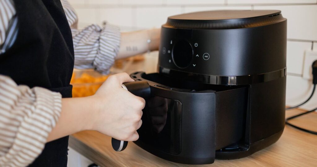 1768699148_0_Close-up-view-of-a-woman-putting-a-basket-into-an-air-fryer-for-cooking.jpg