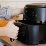 1768699148_0_Close-up-view-of-a-woman-putting-a-basket-into-an-air-fryer-for-cooking.jpg