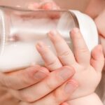 mother-helps-baby-drink-bottle-1049705593.jpg