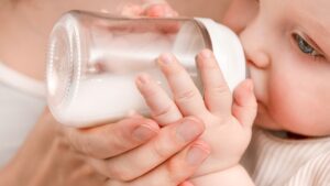 mother-helps-baby-drink-bottle-1049705593.jpg