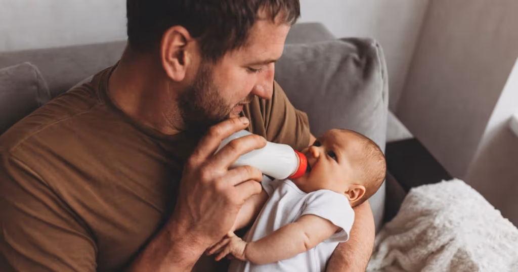 2_family-parenthood-and-people-concept-father-feeding-little-daughter-with-baby-formula-from-bottle.avif