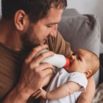 2_family-parenthood-and-people-concept-father-feeding-little-daughter-with-baby-formula-from-bottle.avif
